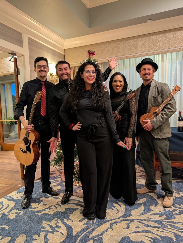 Five acoustic ensemble performers with instruments beside a Christmas tree